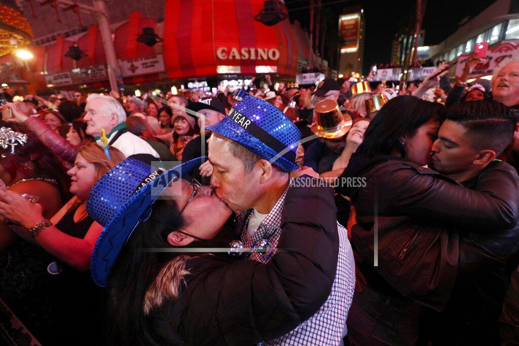 Steve Marcus FILE - In this Jan. 1, 2018, file photo, newlyweds Alison and Kenny Finchum, lower left, of Tulsa, Okla., kiss just after midnight during a New Year's party at the Fremont Street Experience in downtown Las Vegas. Plans for a 14,000-person New Year's Eve street party at canopied casino-mall in Las Vegas are facing pushback from state and local officials, who worry Nevada hospitals may not be able to withstand a potential "superspreader" event. (Steve Marcus/Las Vegas Sun via AP, File)