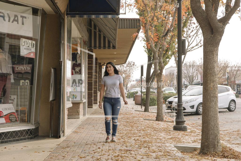 Madeline Tolle Alexandra Orozco walks down the main street of Delano, Calif., on Sunday, Dec. 6, 2020. Just over a two-hour drive from Los Angeles, the population of Delano is roughly 50,000, and jobs are scarce, she says. (Madeline Tolle/The Fuller Project via AP)