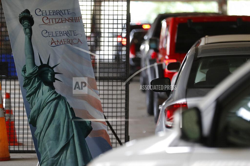 In this June 26, 2020, photo cars line up during a drive-thru naturalization service in a parking structure at the U.S. Citizenship and Immigration Services headquarters on Detroit's east side. The ceremony is a way to continue working as the federal courthouse is shut down due to Coronavirus. The U.S. has resumed swearing in new citizens but the oath ceremonies aren't the same because of COVID-19 and a budget crisis at the citizenship agency threatens to stall them again. (AP Photo/Carlos Osorio)