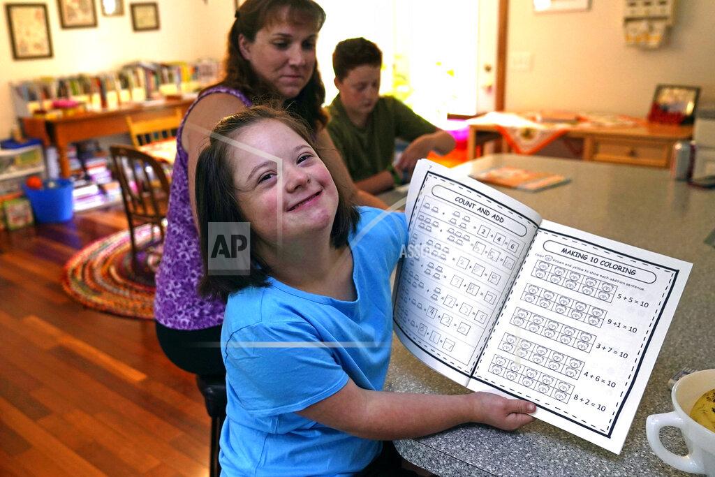 Charles Krupa Lily Osgood, 7, who has Down syndrome, shows off her completed work with her mother, Jennifer, and brother, Noah, 12, at their home, Tuesday, July 20, 2021, in Fairfax, Vt. For some families, the switch to homeschooling was influenced by their children’s special needs. Having observed Lily’s progress with reading and arithmetic while at home during the pandemic, Jennifer is convinced homeschooling is the best option for her going forward. (AP Photo/Charles Krupa)