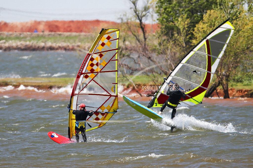 In this April 27, 2020, photo, windsurfers head out from shore on Lake Hefner in Oklahoma City. From Cape Cod to California, festivals are being canceled, businesses in tourist havens are looking at empty reservation books, and people who have been cooped up through a dismal spring are worrying summer will bring just more of the same. (AP Photo/Sue Ogrocki, File)
