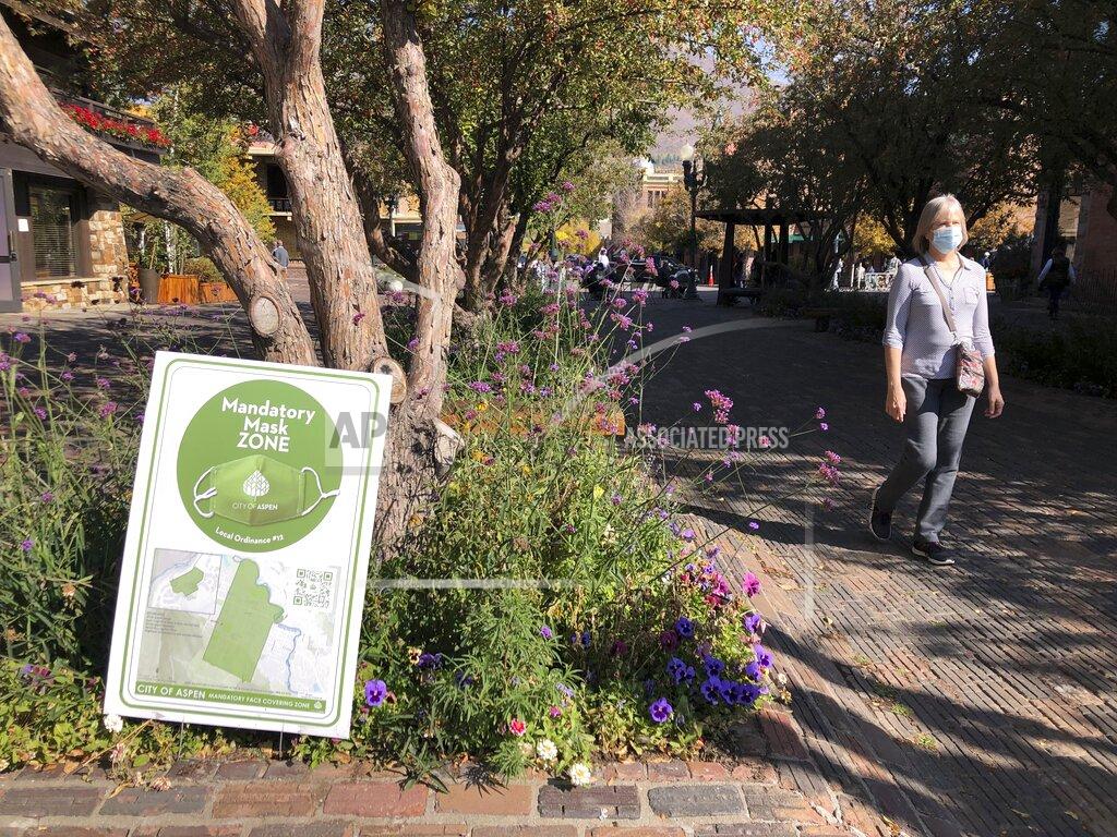 In this Oct. 3, 2020 photo, a pedestrian walks past one of the many signs along the mandatory mask zone in the downtown area in Aspen, Colo. Aspen has taken numerous precautionary measures during the coronavirus pandemic, including mask mandates, occupancy limits in shops and restaurants, and social distancing. (AP Photo/John Marshall)