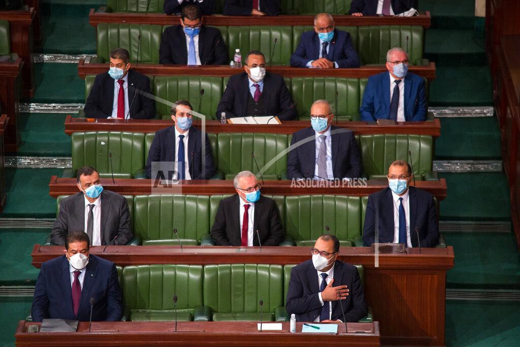 Hassene Dridi Tunisian Prime Minister Hichem Mechichi, first row at right, and designate Justice Minister Youssef Zouaghi, left first row, attend debates as the government faces a confidence vote, Tuesday, Jan.26, 2021 at the Parliament in Tunis. Tunisians are marching on their heavily guarded parliament Tuesday as lawmakers vote on a new government, after a week of youth protests and riots over poverty and lack of jobs that left one young demonstrator dead and hundreds jailed. Prime Minister Hichem Mechichi announced a government reshuffle last week in the midst of the unrest. (AP Photo/Hassene Dridi)