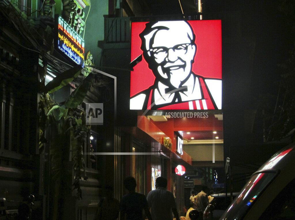 Elaine Kurtenbach FILE - In this Oct. 7, 2016, file photo, a sign of KFC's grinning Colonel Sanders and his goatee is lit outside its outlet in Yangon, Myanmar. The military coup in Myanmar is unlikely to do the country’s struggling economy any good at all. The country once considered a promising last frontier has languished as the pandemic added to its challenges. (AP Photo/Elaine Kurtenbach, File)