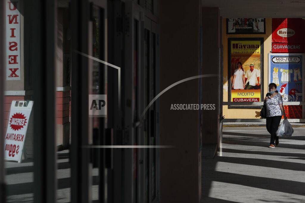 Rebecca Blackwell FILE- In this Oct. 28, 2020, file photo, a woman walks past store publicity on Calle Ocho in the Little Havana section of Miami. Defying fears of another slowdown, U.S. businesses kept hiring at a solid pace in October yet there are signs they remain cautious about the economy's future as the pandemic worsens. (AP Photo/Rebecca Blackwell, File)