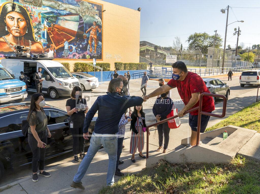 Damian Dovarganes California Gov. Gavin Newsom, front left, greets resident Israel Ortiz, right, after Newsom visited a mobile vaccination site at Ramona Gardens Recreation Center in Los Angeles on Sunday, Feb. 21, 2021. California's new system of delivering and scheduling coronavirus vaccines is being rolled out in select counties. (AP Photo/Damian Dovarganes)