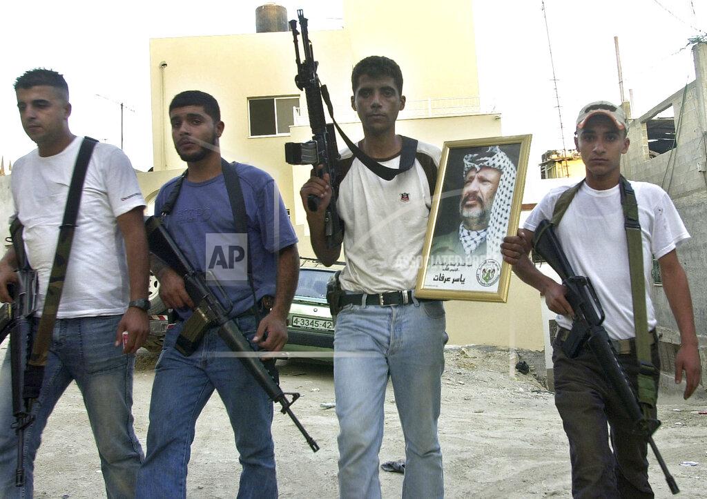 Mohammed Ballas FILE - In this July 31, 200 file photo, Palestinian Zakaria Zubeidi, then leader of the Al-Aqsa Martyrs' Brigades militant group in the West Bank town of Jenin, holds a picture of Yasser Arafat, as he poses with other militants after they set the town's Governorate on fire overnight. For nearly two decades, Zubeidi has been an object of fascination for Israelis and Palestinians alike, who have seen his progression from a child actor to a swaggering militant, to the scarred face of a West Bank theater promoting “cultural resistance” to Israeli occupation. In his latest act, he has emerged as one of Israel's most wanted fugitives after tunneling out of a high-security prison on Monday, Sept. 6, 2021 with five other Palestinian militants. (AP Photo/Mohammed Ballas, File)