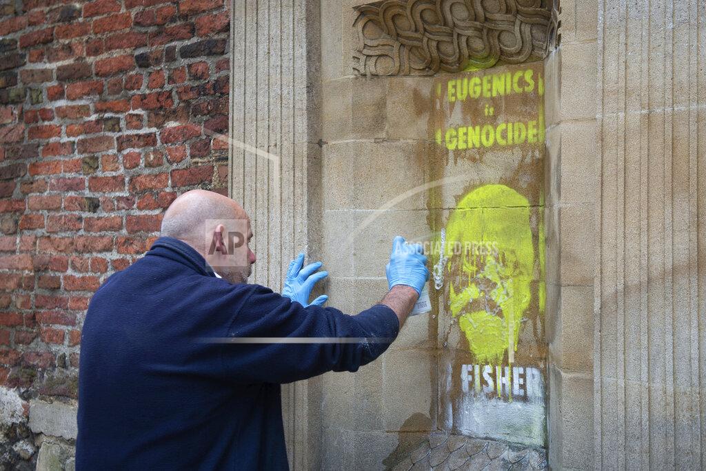 Aaron Chown A man tries to remove a spray painted writing "Eugenics is genocide. Fisher must fall" on Ronald Fisher, founder of the Cambridge Eugenics society, by activists on the Gate of Honor, of Cambridge University, in Cambridge, Britain, Friday, June 12, 2020, following Black Lives Matter protests that took place across the UK over the weekend. The protests were ignited by the death of George Floyd, who died after he was restrained by Minneapolis police on May 25. (Aaron Chown/PA via AP)