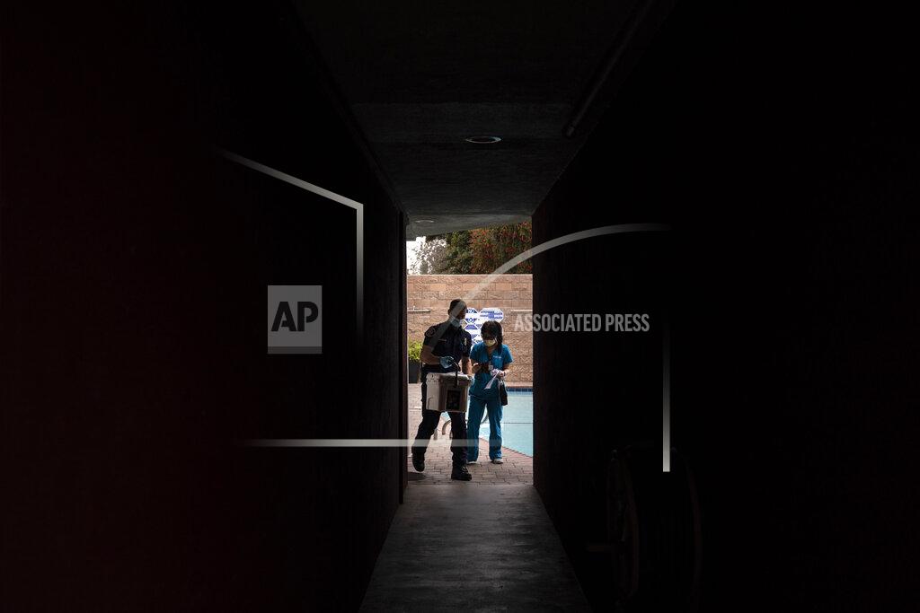Jae C. Hong Pharmacist Stella Kim, right, and Torrance firefighter Trevor Borello leave an apartment building after administering the Pfizer COVID-19 vaccine to two sisters who have muscular dystrophy, Wednesday, May 12, 2021, in Torrance, Calif. Teamed up with Torrance Fire Department, Torrance Memorial Medical Center started inoculating people at home in March, identifying people through a city hotline, county health department, senior centers and doctor's offices, said Mei Tsai, the pharmacist who coordinates the program. (AP Photo/Jae C. Hong)