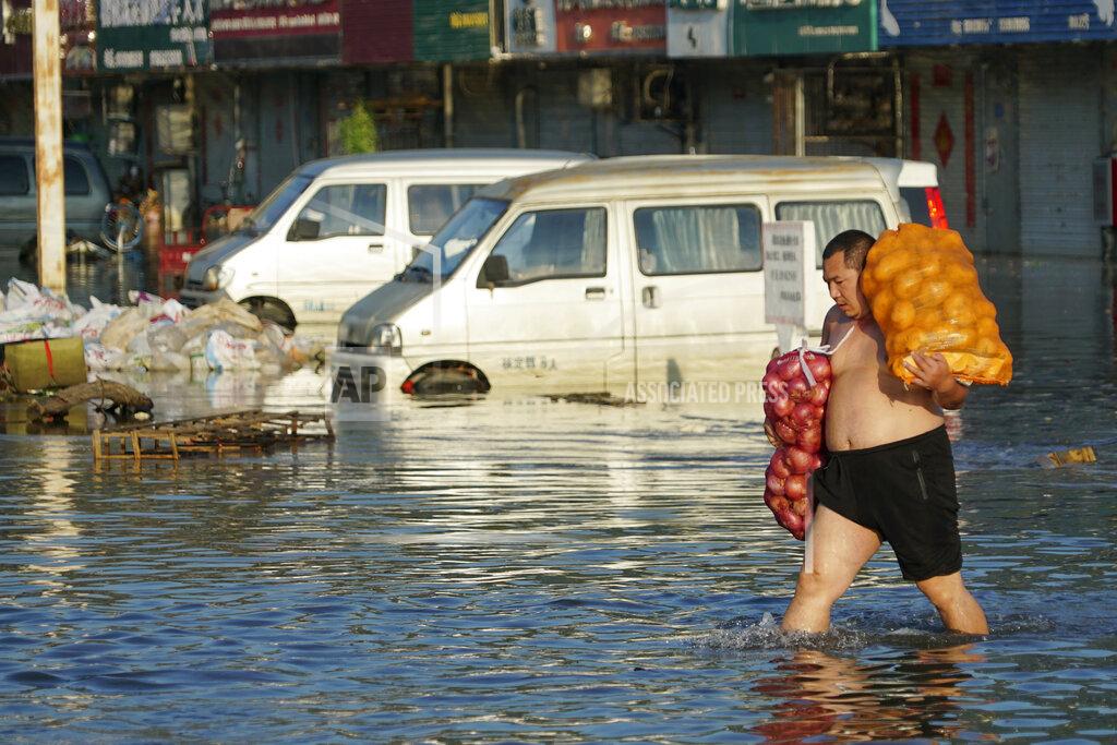 Dake Kang FILE - In this Monday, July 26, 2021 file photo, a man carries bags of onions out of the flooded Yubei Agricultural and Aquatic Products World in Xinxiang in central China's Henan Province. Scientists say there’s something different this year from the recent drumbeat of climate weirdness. This summer a lot of the places hit by weather disasters are not used to getting extremes and many of them are wealthier, which is different from the normal climate change victims. That includes unprecedented deadly flooding in Germany and Belgium, 116-degree heat records in Portland, Oregon and similar blistering temperatures in Canada, along with wildfires. Now Southern Europe is seeing scorching temperatures and out-of-control blazes too. And the summer of extremes is only getting started. Peak Atlantic hurricane and wildfire seasons in the United States are knocking at the door. (AP Photo/Dake Kang, File)