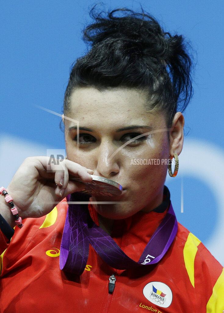 FILE - In this file photo dated Wednesday, Aug. 1, 2012, Silver medalist Roxana Cocos of Romania kisses her medal during a medals ceremony after the women's 69-kg, weightlifting competition at the 2012 Summer Olympics, in London. A culture of alleged corruption among international weightlifting officials has been detailed in a 50-page investigative report released Thursday June 24, 2021, of covered-up doping cases, with Cocos stripped of her medal years later when re-tests revealed her steroid use. (AP Photo/Hassan Ammar, FILE)