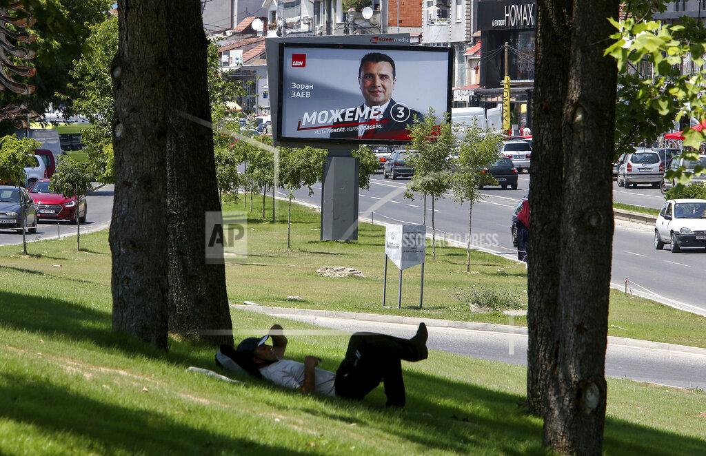 Boris Grdanoski A man rests under a tree near an electoral poster of the leader of the ruling Social Democrats Zoran Zaev, in a street in Skopje, North Macedonia on Saturday, July 11, 2020. North Macedonia holds its first parliamentary election under its new country name this week, with voters heading to the polls during an alarming spike of coronavirus cases in the small Balkan nation. (AP Photo/Boris Grdanoski)