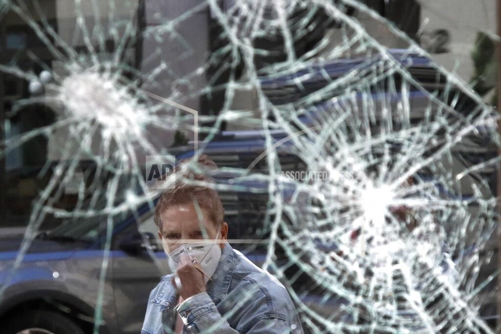 Elise Amendola FILE - In this Monday, June 1, 2020 file photo, a woman wearing a mask due to coronavirus concerns, looks at a smashed storefront window in Boston's Downtown Crossing. The destruction caused by vandals and looters in cities across the country, who struck as demonstrators took to the streets in reaction to the killing of George Floyd in Minneapolis, has devastated small businesses already reeling from the coronavirus outbreak. (AP Photo/Elise Amendola, File)