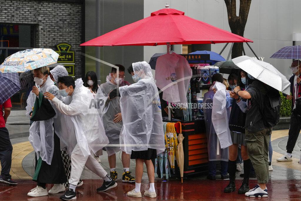 Andy Wong Visitors wearing face masks to help protect themselves from the coronavirus purchase raincoats from a store at the Universal Studios Beijing in Beijing, Monday, Sept. 20, 2021. Thousands of people brave the rain visit to the newest location of the global brand of theme parks which officially opens on Monday. (AP Photo/Andy Wong)