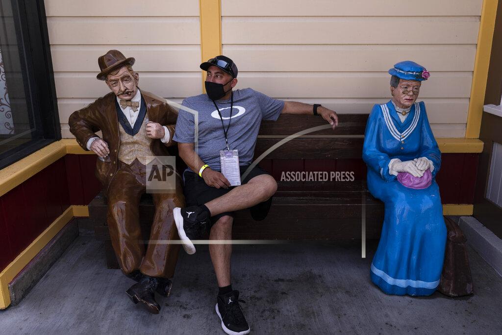 Jae C. Hong A visitor, who declined to give his name, rests on a bench with two figures during the Knott's Taste of Boysenberry Festival at Knott's Berry Farm in Buena Park, Calif., Tuesday, March 30, 2021. Massive Los Angeles County can reopen even more businesses, California public health officials announced Tuesday. The county of 10 million people was one of several counties, including neighboring Orange County, that moved into the state's second-least restrictive orange tier amid low coronavirus case rates. (AP Photo/Jae C. Hong)