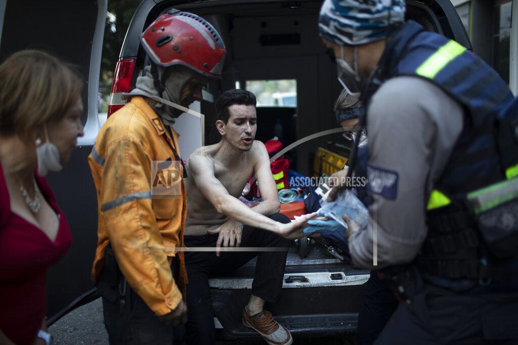Ariana Cubillos Angels of the Road volunteer paramedics tend to a man's injuries after his car caught fire at a parking lot in Caracas, Venezuela, Monday, Feb. 8, 2021. Despite receiving no paychecks, the roughly 40 volunteer paramedics of Angels of the Road are ready at a moment's notice to jump onto motorcycles and fire up their single ambulance and race into the streets to attend an emergency. (AP Photo/Ariana Cubillos)