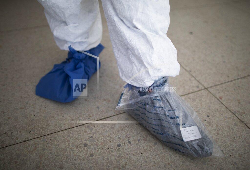 Ariana Cubillos A security worker uses a plastic bag over one of his shoes before going into the COVID-19 wing of the José Gregorio Hernández Hospital, a public hospital in the Catia neighborhood of Caracas, Venezuela, Saturday, Oct. 10, 2020. Two security guards at the COVID-19 entrance say they fought through COVID-19 symptoms, and borrow protective clothing from other hospital workers. (AP Photo/Ariana Cubillos)
