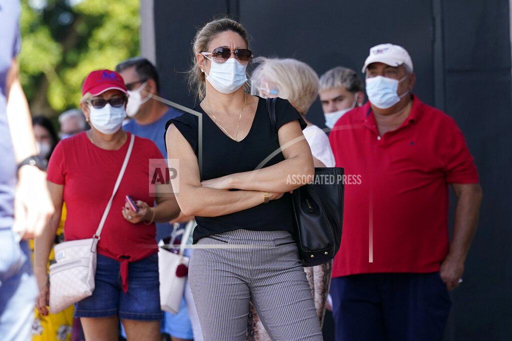 People stand in line for early voting at the John F. Kennedy Library, Tuesday, Oct. 27, 2020, in Hialeah, Fla. Masks are required at some polling places around the country and strongly encouraged in most others as a basic precaution to help keep poll works and others safe from the fast-spreading coronavirus. But mandates tying a face covering to casting a ballot are sure to lead to confrontations on Election Day, and those will almost certainly grab wide attention if they arise in any of the presidential battleground states. (AP Photo/Lynne Sladky)