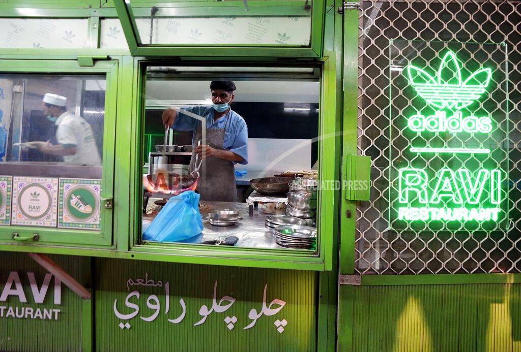 Kamran Jebreili With new Adidas - Ravi sign is displayed wall as a cook prepares food at Ravi restaurant in Satwa district of Dubai, United Arab Emirates, Wednesday, June 22, 2022. Adidas has teamed up with Dubai nostalgic family-owned Pakistani restaurant to release the Superstar Ravi sneaker. (AP Photo/Kamran Jebreili)
