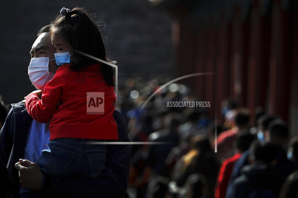 Andy Wong A man holds a child, both wearing face masks to help curb the spread of the coronavirus line up with visitors to enter an exhibition held at the Forbidden City in Beijing, Saturday, Nov. 7, 2020. China on Saturday reported 33 new confirmed coronavirus infections, all of which the National Health Commission said were in patients who contracted the virus abroad. (AP Photo/Andy Wong)