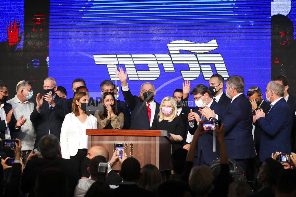 Ariel Schalit Israeli Prime Minister Benjamin Netanyahu, center, wearing a protective face mask, waves after delivering a speech to supporters following the announcement of exit polls of the Israeli parliamentary elections at his party's headquarters in Jerusalem, Wednesday, March. 24, 2021. (AP Photo/Ariel Schalit)