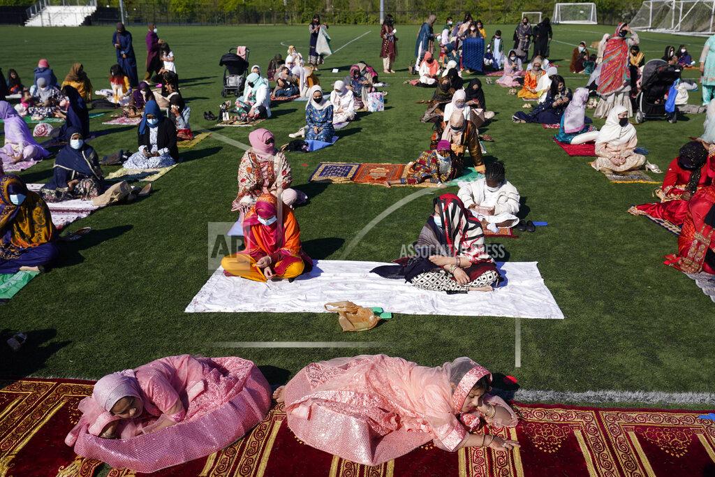 Seth Wenig Aqsa Syeda, 8, left front, and her cousin Ameena Ahmed, 9, right front, relax before the start of Eid al-Fitr prayers in Overpeck County Park in Ridgefield Park, N.J., Thursday, May 13, 2021. Millions of Muslims across the world are marking a muted and gloomy holiday of Eid al-Fitr, the end of the fasting month of Ramadan - a usually joyous three-day celebration that has been significantly toned down as coronavirus cases soar. (AP Photo/Seth Wenig)