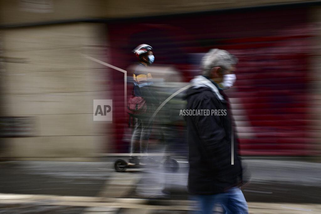 A pedestrian and a person using a scooter wear face mask protection to prevent the spread of COVID-19 during an autumn day in Pamplona, northern Spain, Friday, Sept. 25, 2020. (AP Photo/Alvaro Barrientos)