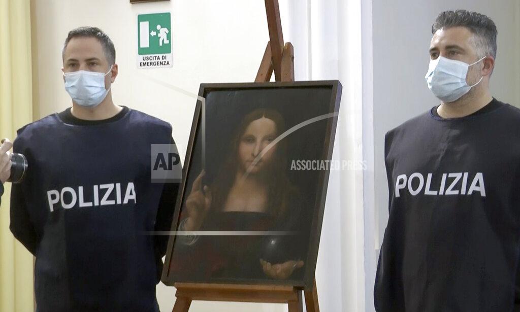 Sicomunicazione In this image taken from a video, two police officers pose by a copy of the “Salvator Mundi” (Savior of the World), by Leonardo da Vinci, in Naples, Italy, Wednesday, Jan. 20, 2021. Italian police have recovered a copy of Leonardo da Vinci’s 16th century “Salvator Mundi” painting of Jesus Christ that was stolen from a Naples church without the priests even realizing it was gone. The discovery was made over the weekend when Naples police working on a bigger operation found the painting hidden in an apartment. Police chief Alfredo Fabbrocini said the owner offered a “less than credible” explanation that he had “casually” bought it at a small market. (AP Photo/Sicomunicazione)