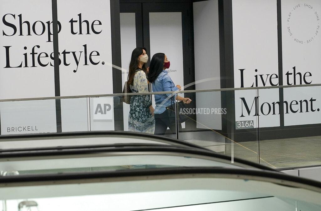 Shoppers walk past a vacant storefront at Brickell City Centre, Friday, Nov. 6, 2020, in Miami. The spread of COVID-19 vaccines will power a stronger global economic recovery in 2021, the International Monetary Fund forecast Tuesday, Jan. 26, 2021. (AP Photo/Lynne Sladky)