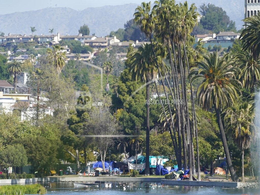 Los Angeles City Sanitation trucks are seen under palm trees around tents set on the north side of Echo Park Lake in Los Angeles Friday, March 26, 2021. A newly installed fence surrounded the park Thursday after a late-night confrontation between police and vocal demonstrators who oppose the city's effort to remove a large homeless encampment and perform extensive repairs of the site. The encampment has been the site of drug overdoses, assaults, and shootings, with four deaths in the park over the past year, according to a statement from City Councilmember Mitch O'Farrell's office. (AP Photo/Damian Dovarganes)
