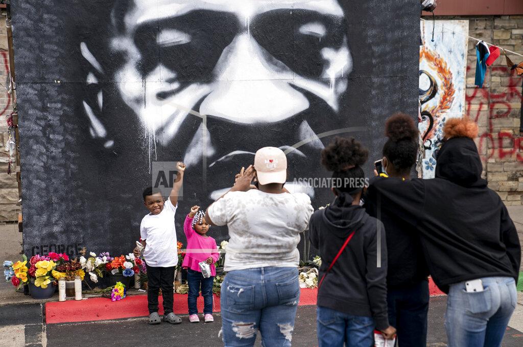 John Minchillo A family takes an image in front of a mural of the deceased George Floyd as demonstrators gather for a solidarity rally in memory of Floyd and Daunte Wright outside Cup Foods, Sunday, April 18, 2021, in Minneapolis. (AP Photo/John Minchillo)