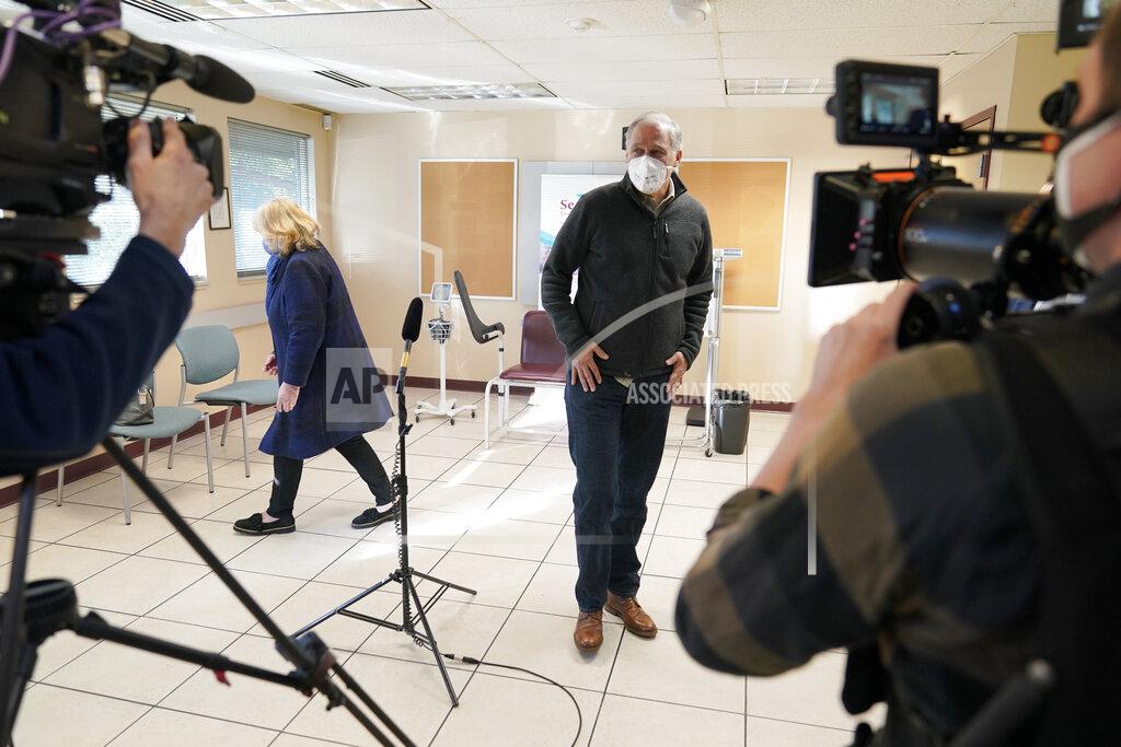Ted S. Warren Washington Gov. Jay Inslee, center, talks to reporters as his wife Trudi, left, stands nearby, after they both were given the first shot of the Moderna COVID-19 vaccine, Friday, Jan. 22, 2021, at a Sea-Mar Community Health Center in Olympia, Wash. (AP Photo/Ted S. Warren)