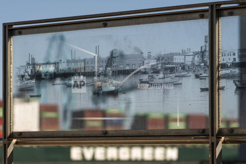 Damian Dovarganes In this Tuesday, Oct. 19, 2021, photo containers stacked on an Evergreen cargo ship are seen through a historical picture of the Port of Los Angeles, part of the Terminal Island Japanese Fishing Village Memorial in San Pedro, Calif. California Gov, Gavin Newsom on Wednesday, Oct. 20, 2021 issued an order that aims to ease bottlenecks at the ports of Los Angeles and Long Beach that have spilled over into neighborhoods where cargo trucks are clogging residential streets. Last week the White House allowed the ports complex to become a 24-hour operation in an effort to break the logjam and reduce shipping delays. (AP Photo/Damian Dovarganes)