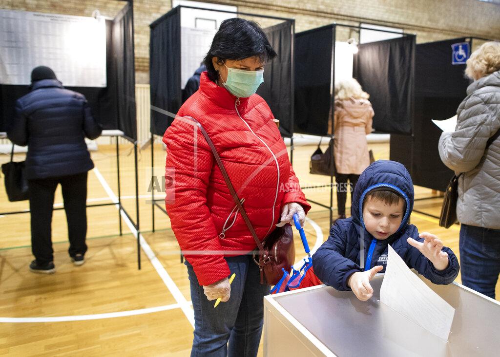 Mindaugas Kulbis A woman with a child casts her ballot at a polling station during parliamentary elections in Vilnius, Lithuania, Sunday, Oct. 11, 2020. Polls opened Sunday for the first round of national election in Lithuania, where voters will renew the 141-seat parliament and the ruling four-party coalition is widely expected to face a stiff challenge from the opposition to remain in office. (AP Photo/Mindaugas Kulbis)