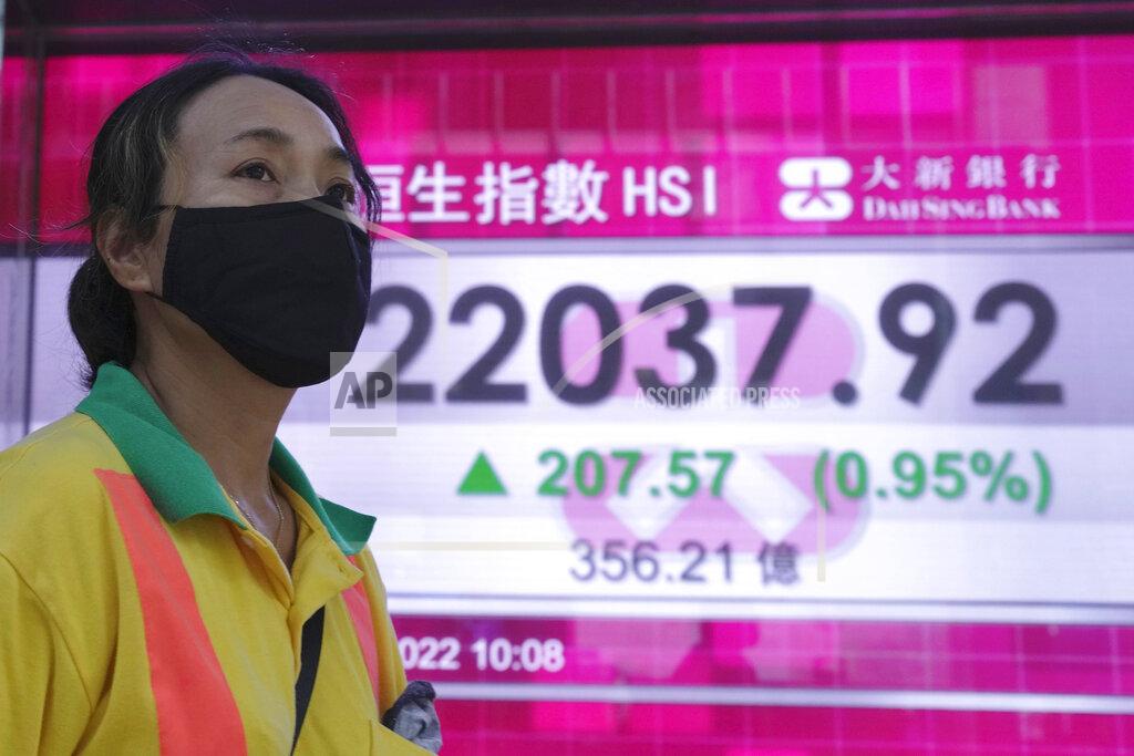 Kin Cheung A woman wearing a face mask walks past a bank's electronic board showing the Hong Kong share index in Hong Kong, Tuesday, July 5, 2022. (AP Photo/Kin Cheung)
