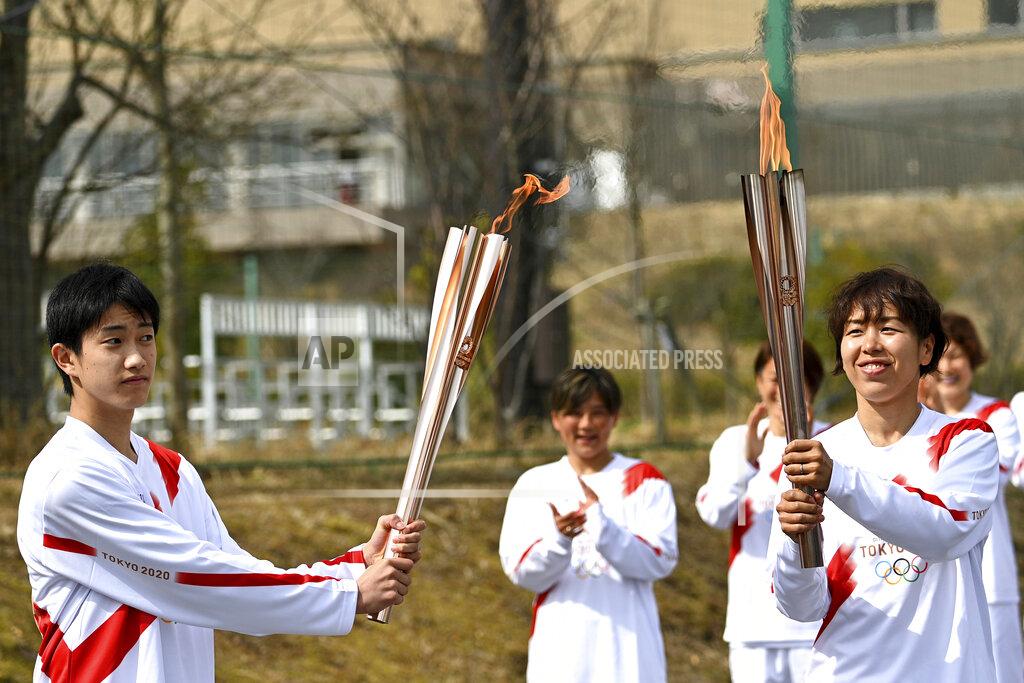 Philip Fong Japanese torchbearer Azusa Iwashimizu, right, a member of Japan women's national football team, passes the Olympic flame to high school student Asato Owada, left, at a torch kiss point during the Tokyo 2020 Olympic Torch Relay grand start outside J-Village National Training Center in Naraha, Fukushima prefecture, northeastern Japan, Thursday, March 25, 2021. The torch relay for the postponed Tokyo Olympics began its 121-day journey across Japan on Thursday and is headed toward the opening ceremony in Tokyo on July 23. (Philip Fong/Pool Photo via AP)