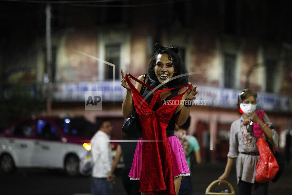 Rebecca Blackwell Sex worker Geraldine, wearing cat make-up, excitedly holds up a dress she is thinking of buying from a street vendor, so that her partner, sitting nearby to keep her company, can see it, as she waits for clients outside the Revolution subway station, in Mexico City, Saturday, March 13, 2021. According to Geraldine, 30, the pandemic has cut clients and increased risks to the sex workers but has also brought out more assistance for them too, both from dedicated organizations such as the activist group Brigada Callejera or "The Street Brigade" and from individuals who have donated food or clothing. (AP Photo/Rebecca Blackwell)