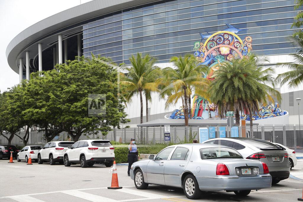 Lynne Sladky Vehicles pass by the home run sculpture as they wait in line outside of Marlins Park at a COVID-19 testing site during the coronavirus pandemic, Monday, July 6, 2020, in Miami. The long line of cars each morning as players arrive at work provides a reminder of the risks when they leave. Behavior away from the ballpark will be a big factor in determining whether Major League Baseball's attempt to salvage the 2020 season can succeed. (AP Photo/Lynne Sladky)