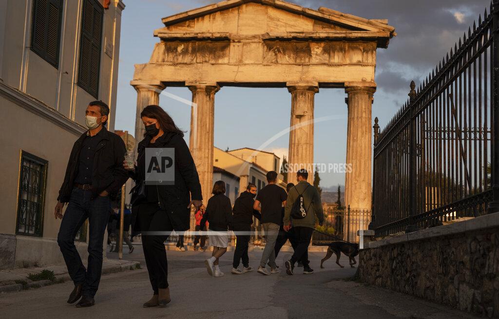 People wearing protective face masks walk in front the Gate of the ancient Roman agora, in Plaka, district of Athens, on Tuesday, April 6, 2021. Lockdown measures have been in force since early November but an ongoing surge in COVID-19 infections remains high as the country battles to emerge from deep recession. (AP Photo/Petros Giannakouris)