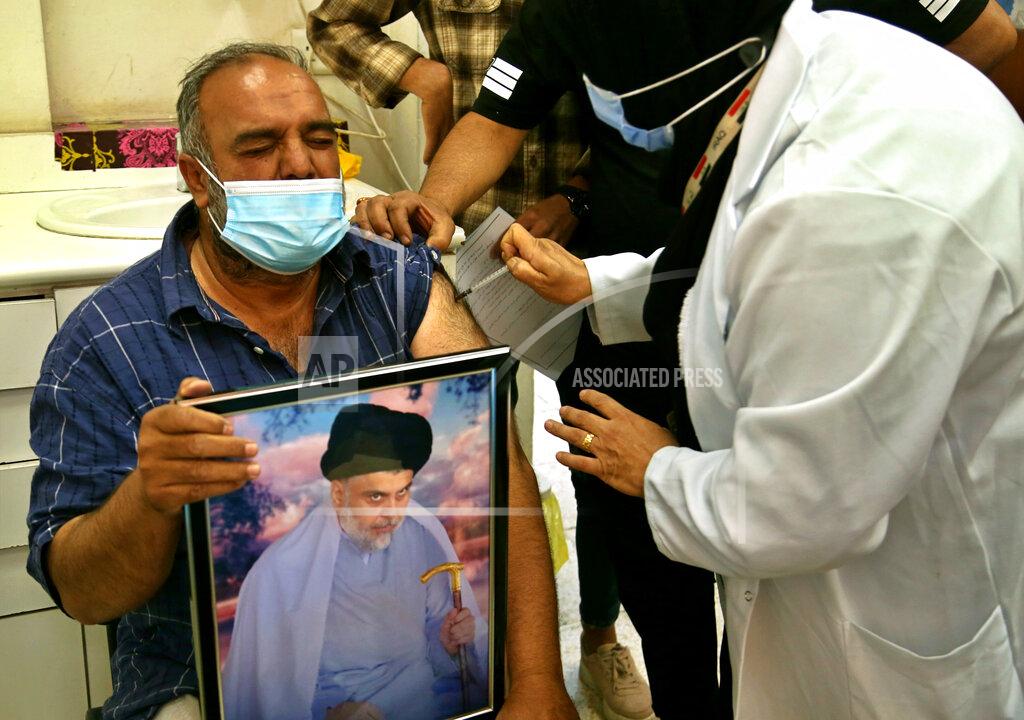 Hadi Mizban A follower of populist Shiite cleric Muqtada al-Sadr holds a picture of him while receiving a dose of the Chinese Sinopharm coronavirus vaccine at a clinic in Sadr City, Baghdad, Iraq, Wednesday, May 4, 2021. Iraq’s vaccine rollout had been faltering for weeks. Apathy, fear and rumors kept many from getting vaccinated despite a serious surge in coronavirus infections and calls by the government for people to register for shots. It took al-Sadr’s public endorsement of vaccinations — and images of him getting the shot — to turn things around. (AP Photo/Hadi Mizban)