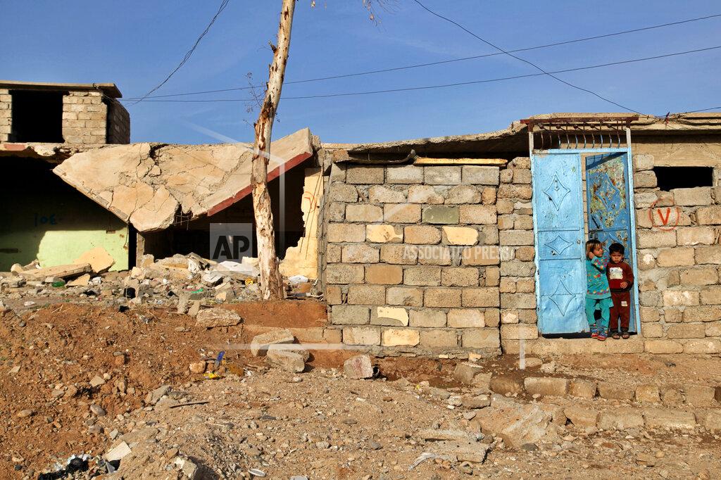Children stand outside the ruins of their home, in the Hay Tanak slum of Mosul, Iraq, Nov. 28, 2020. A push by the Iraqi government to close displacement camps by the end of the year threatens to leave tens of thousands of people homeless and without aid during a pandemic and at the onset of winter. The displaced were driven from their homes during the war against the Islamic State group and many say they cannot return because their homes were destroyed or they fear reprisal by tribes and militias. Aid groups say the haphazard implementation of the policy is fueling more displacement and resentment. (AP Photo/Samya Kullab)