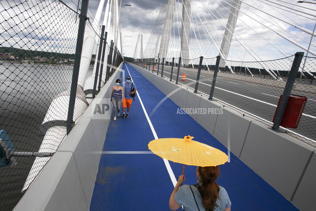 A woman carries a parasol as she walks on the Gov. Mario M. Cuomo Bridge bike and pedestrian path on its opening day, Monday, June 15, 2020 in Tarrytown, N.Y. The new 3.6 mile path runs from Tarrytown across the Hudson River to South Nyack, N.Y. (AP Photo/Mark Lennihan)