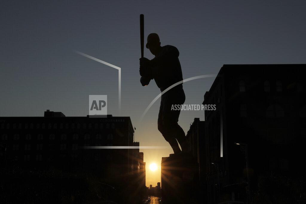 Jeff Roberson The sun sets in the distance as a statue of St. Louis Cardinals great Stan Musial stands outside a quiet Busch Stadium Friday, Aug. 7, 2020, in St. Louis. Major League Baseball announced Friday that a three-game series between the Chicago Cubs and Cardinals set for this weekend in St. Louis has been postponed after two more Cardinals players and a staff member tested positive for the coronavirus. (AP Photo/Jeff Roberson)