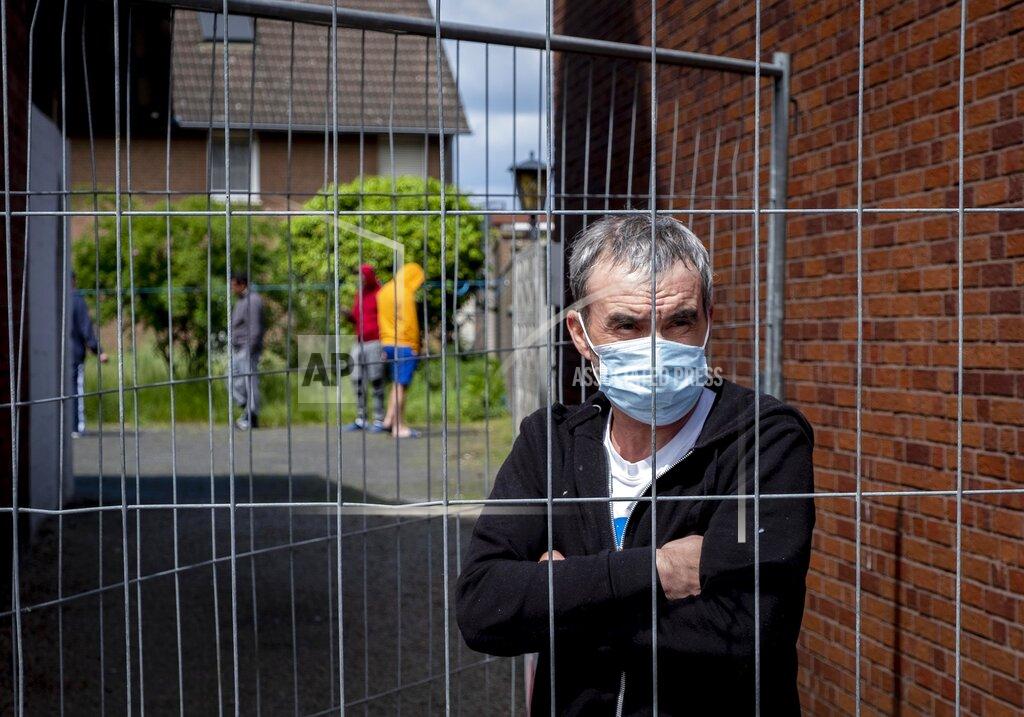 Michael Probst FILE - In this Tuesday, May 12, 2020 file photo, Iulian, Romanian worker who stands behind the fence that was set up at the entrance of a housing of Romania slaughterhouse workers in Rosendahl, Germany. Hundreds of the workers were tested positive on the coronavirus and were put on quarantine.More than 50,000 people have died after contracting COVID-19 in Germany, a number that has risen swiftly over recent weeks as the country has struggled to bring down infection figures. (AP Photo/Michael Probst, file)