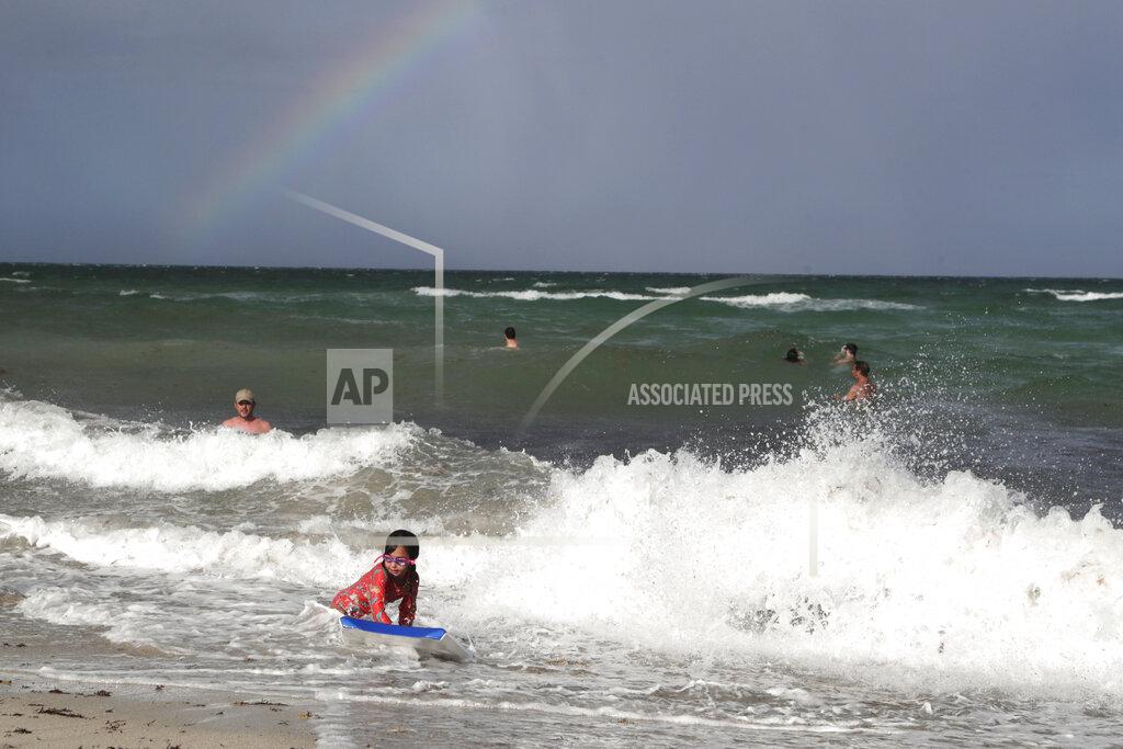 Lynne Sladky A rainbow is seen on the horizon as people enjoy the waves from a high surf, Friday, July 31, 2020, in Miami Beach, Fla. Forecasters declared a hurricane warning for parts of the Florida coast Friday as Hurricane Isaias drenched the Bahamas on track for the U.S. East Coast. (AP Photo/Lynne Sladky)