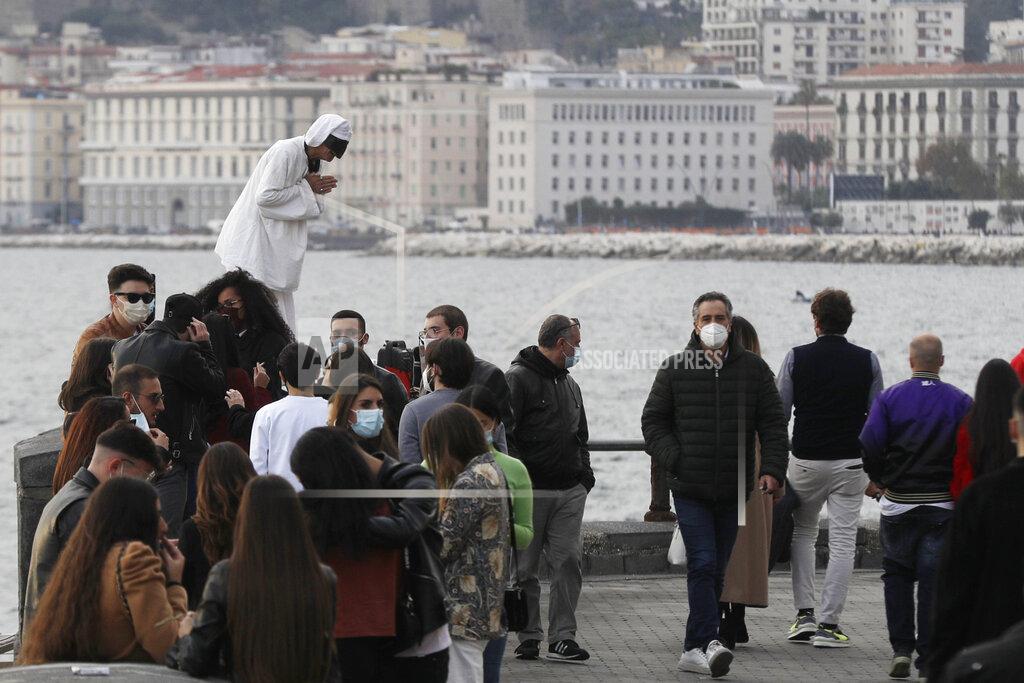 Gregorio Borgia People stroll along Viale Caracciolo overlooking the Gulf of iNaples, Italy, Saturday, Nov. 14, 2020. Along the Naples waterfront, Luigi Orefice perched his 4-year-old son, Giovanni, on the thick wall lining the promenade. With fog ringing the Vesuvius volcano in the background, the postcard-like panorama would be familiar to tourists. But his job delivering beverages to hospitals lets Orefice see the ugly realities beyond the “O Sole Mio” image tourists might have of the south. (AP Photo/Gregorio Borgia)