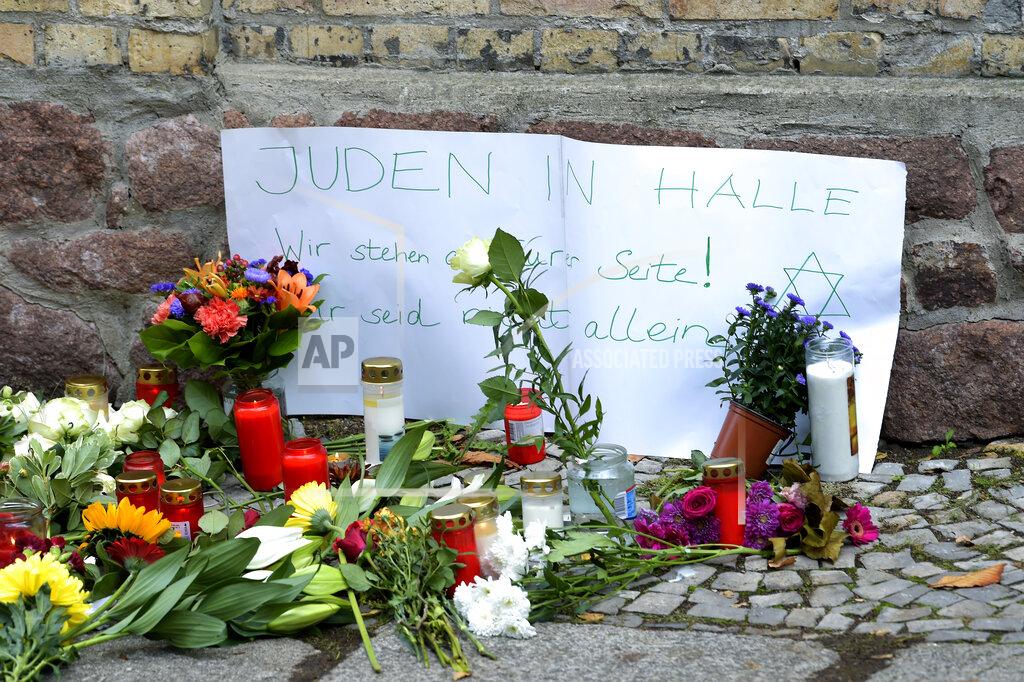 FILE -- In this Oct. 10, 2019 file photo, candles and flowers are placed in front of a synagogue in Halle, Germany after a heavily armed assailant ranting about Jews tried to force his way into the synagogue in Germany on Yom Kippur, Judaism's holiest day, then shot two people to death nearby in an attack. Sign reads, "Jews in Halle - We stay next to you! You are not alone." Israeli researchers in their annual report released Monday, April 20, 2020, reported that the global outbreak of the coronavirus has sparked a rise in anti-Semitic expression blaming the Jews for the spread of the disease and the economic recession it has caused. (AP Photo/Jens Meyer, File),