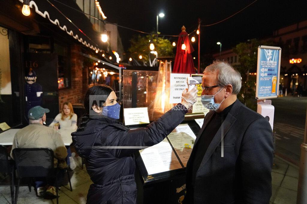 Marcio Jose Sanchez A hostess takes a customer's temperature at Ye Olde King's Head on Thursday, Nov. 19, 2020, in Santa Monica, Calif. The British restaurant and bar in seaside Southern California has been battered the past nine months and was in the process of adapting to new restrictions that took effect Friday, Nov. 20 that would further crimp its recovery even as the prospect of a stay-home order loomed that could cripple the business. (AP Photo/Marcio Jose Sanchez)