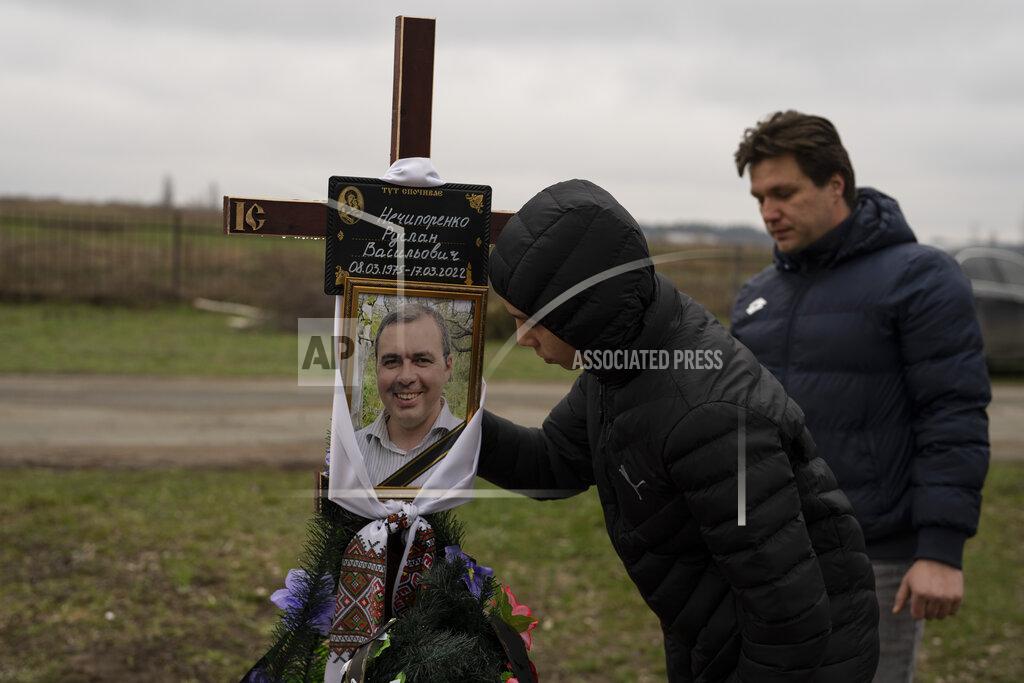 Petros Giannakouris Yura Nechyporenko, 15, kisses the pictures of his father Ruslan Nechyporenko in front of his uncle Andriy Nechyporenko, at the cemetery in Bucha, on the outskirts of Kyiv, Ukraine, on Thursday, April 21, 2022. The teen survived an execution attempt by Russian soldiers while his father was killed, and now his family seeks justice. (AP Photo/Petros Giannakouris)
