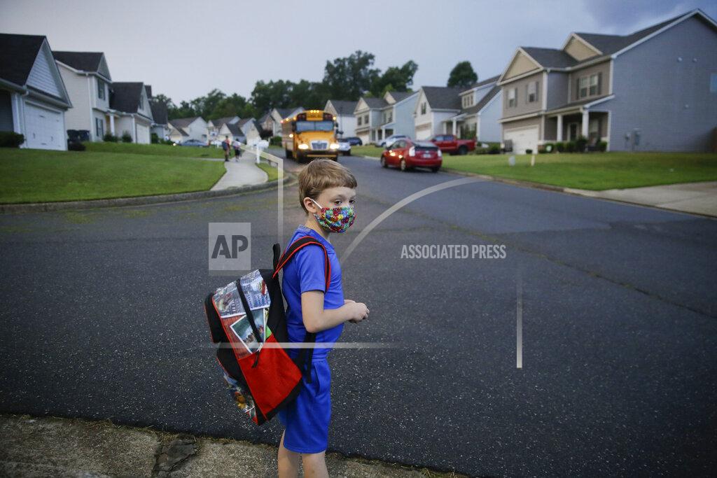 Brynn Anderson CORRECTS LAST NAME TO ADAMUS, NOT ADAMS - Paul Adamus, 7, waits at the bus stop for the first day of school on Monday, Aug. 3, 2020, in Dallas, Ga. Neighboring states arrived at differing conclusions on who’s in charge of the reopening of schools. The differences in philosophy underscore some of the difficulties facing states as they grapple with how to proceed amid growing coronavirus infections in numerous states. (AP Photo/Brynn Anderson)